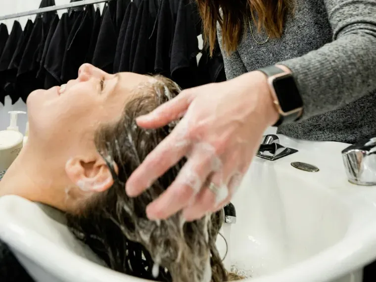 A stylist washing a client's hair at the basin